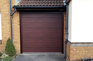 A Carteck Center Rib sectional garage door in Mahogany wood finish with a matching frame, fitted within the opening. The frame has a Rosewood UPVC trim around it to finish it. Garage door fitted in Bracknell, Berkshire.