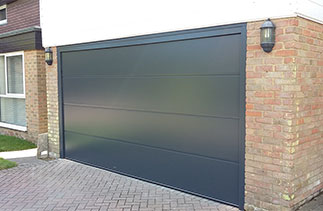 A Carteck solid ribbed style sectional garage door in Anthracite with a Anthracite painted frame and Anthracite UPVC. This door and frame was fitted between the brick opening to cover the old mastic lines and untidy brick work and to avoid having to clad the inside brick faces with large slabs of UPVC. By fitting it this way it also covered the garage floor which would have been visible if the frame was fitted behind the opening. Door fitted in Ascot, Berkshire.