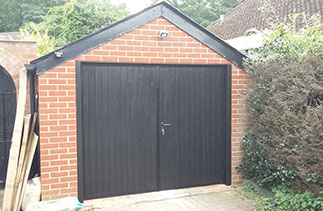A set of Grp Black wood grain side hinged garage doors fitted with two Black timber posts. Fitted in Mytchett, Surrey.